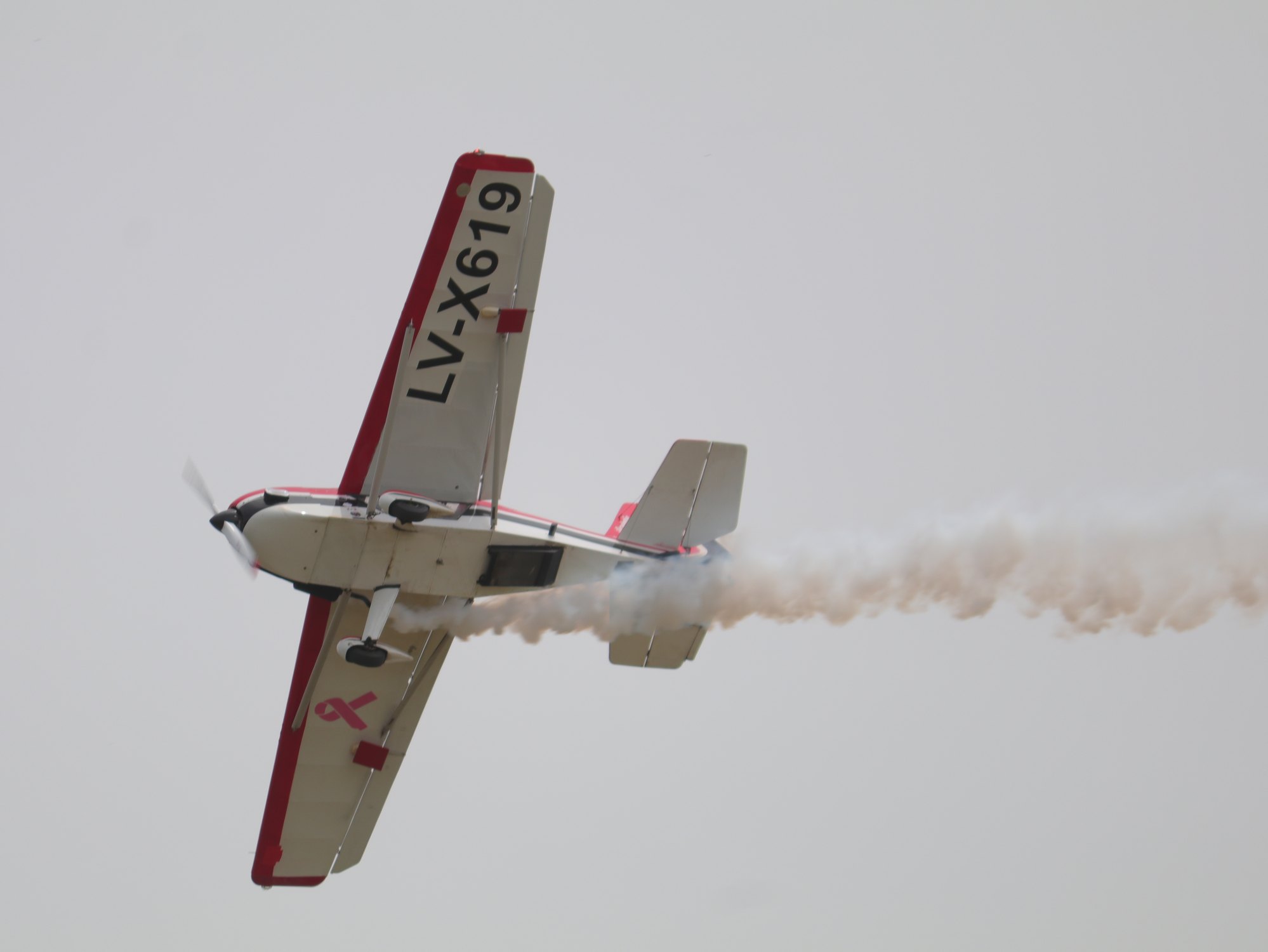 Aeronave acrobatica roja realizando un giro con estela de humo